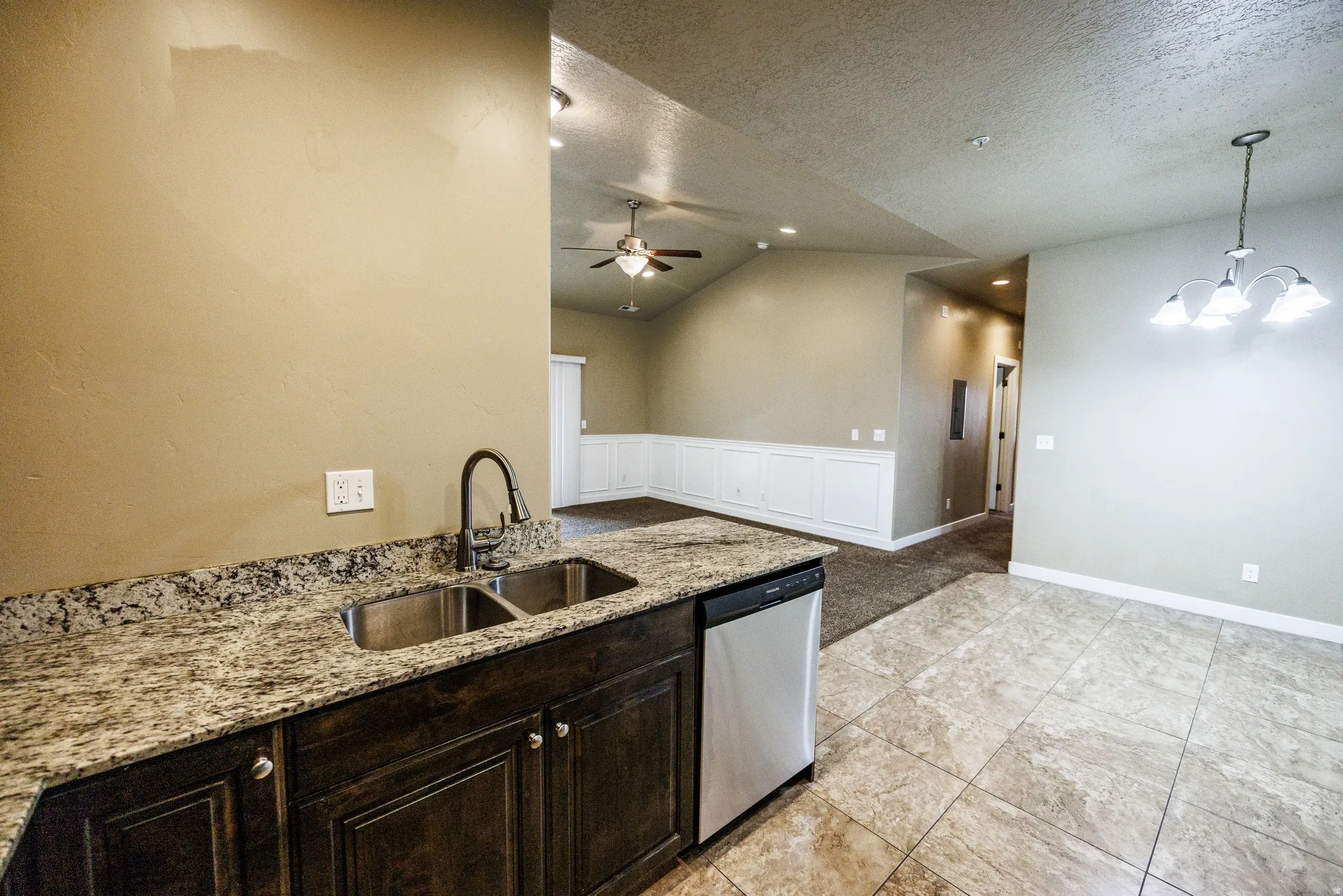 Kitchen area featuring granite-style countertops, an undermount double-basin sink with a gooseneck faucet, dark wood-finish cabinetry, and a stainless steel dishwasher