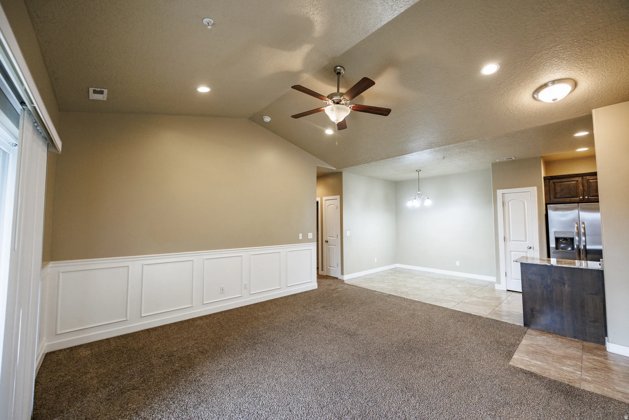 Open-concept living area featuring vaulted ceilings, recessed lighting, a ceiling fan, and decorative wainscoting