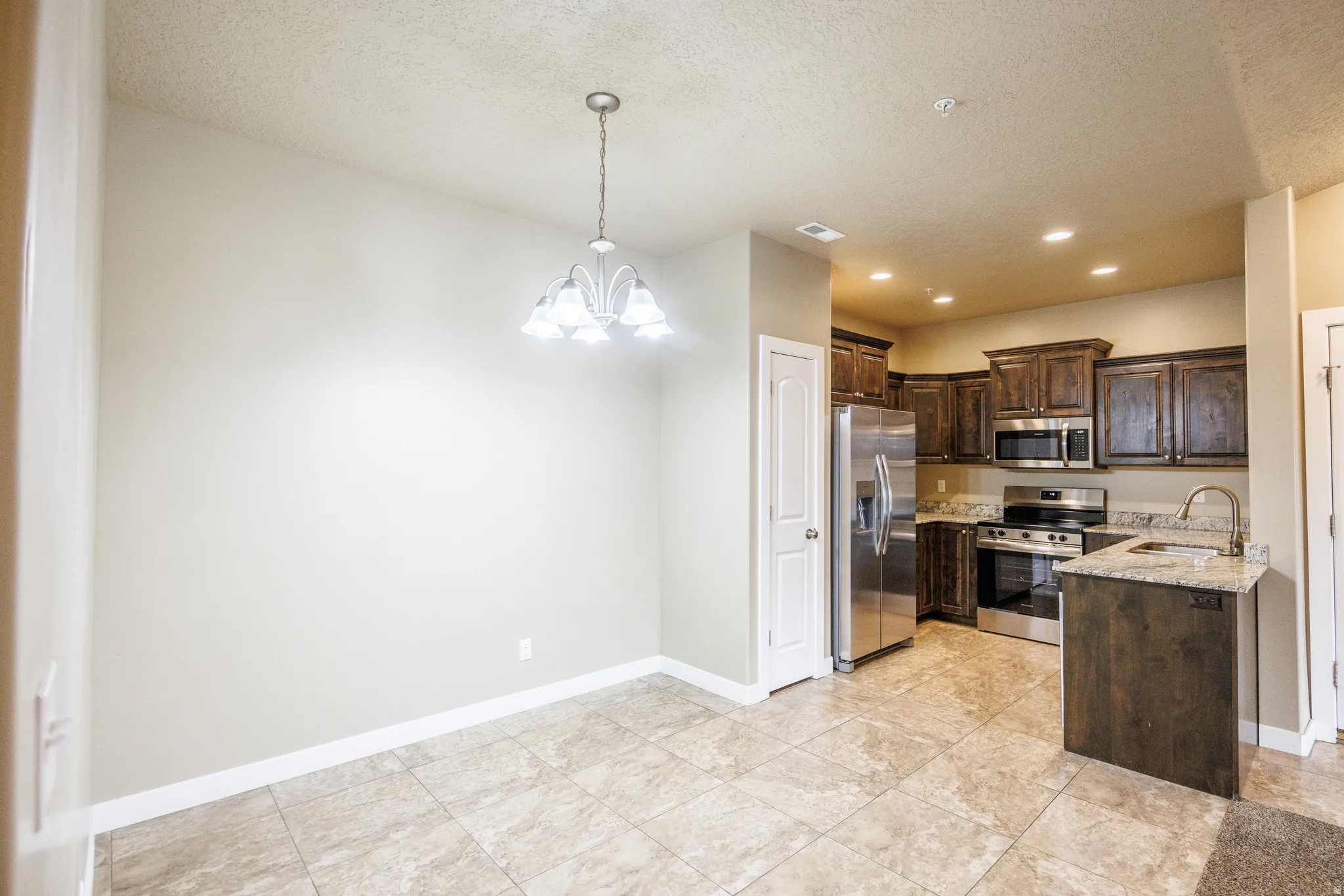 Kitchen and dining area featuring tile flooring, dark wood cabinetry, stainless steel appliances, granite countertops, and a ceiling-mounted chandelier