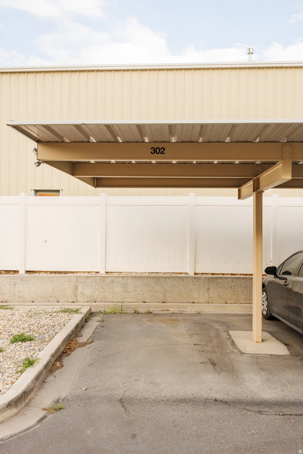 Covered parking space #302 featuring a metal roof structure, concrete support beams, and an asphalt surface