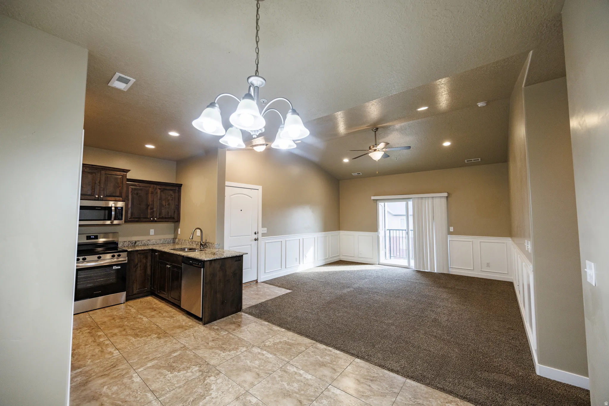 Open-concept living area featuring a kitchen with stainless steel appliances, dark wood cabinetry, and granite-style countertops