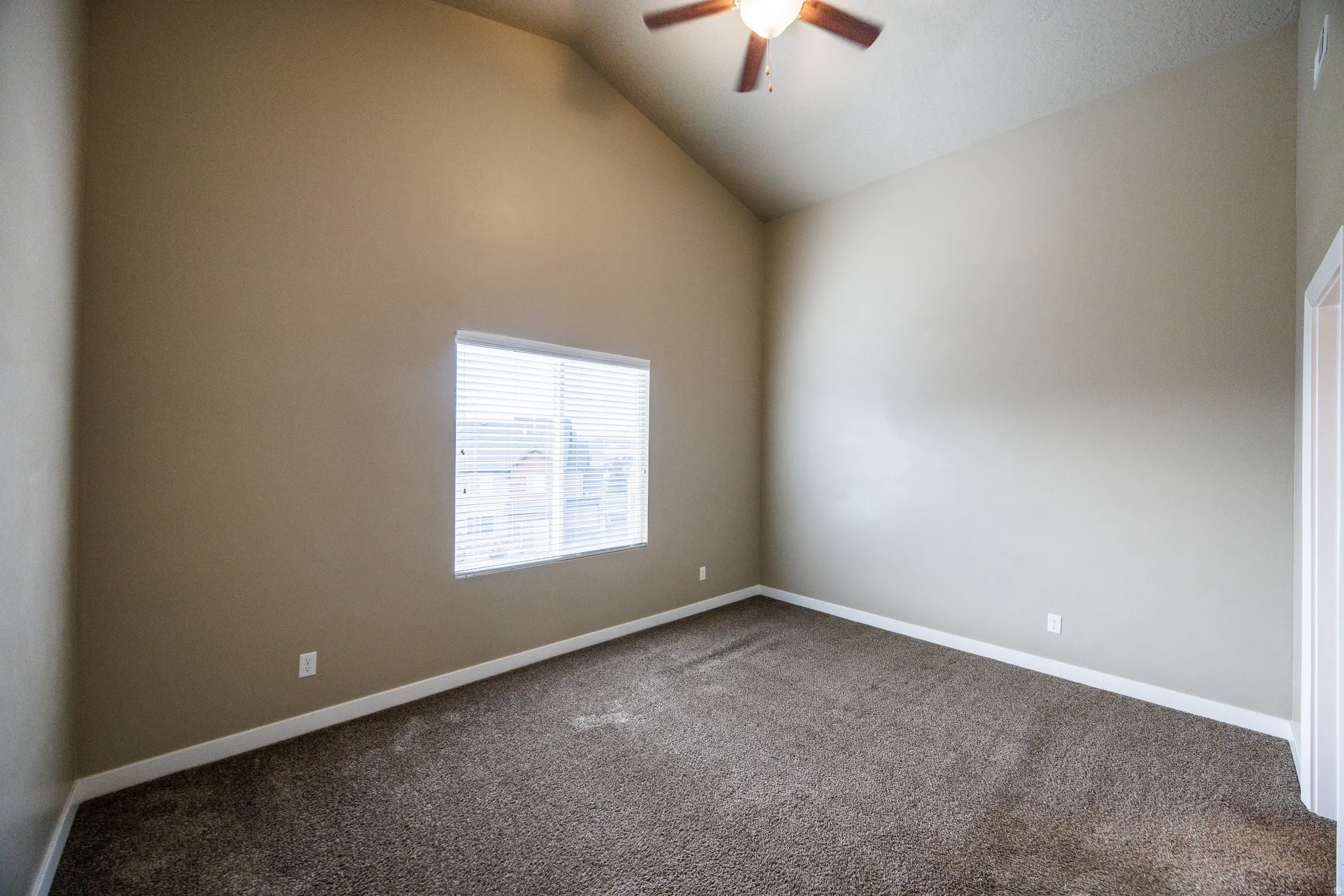 Vaulted ceiling room featuring a ceiling fan with light fixture, neutral-toned walls, and textured carpeting