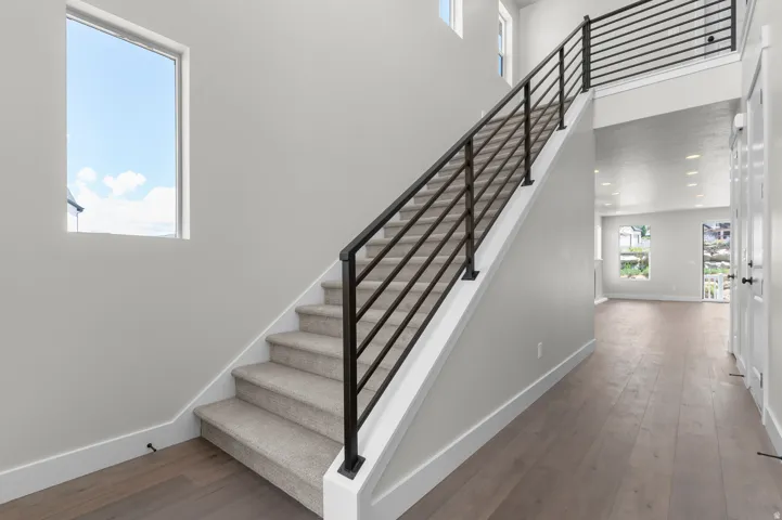 Two-story entryway featuring wood-finish flooring, a carpeted staircase with contemporary horizontal black railings, and light gray walls