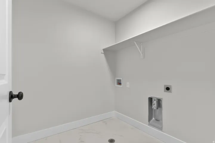 Dedicated laundry area featuring a white shelving unit, light gray walls, white baseboards, and marble-look flooring