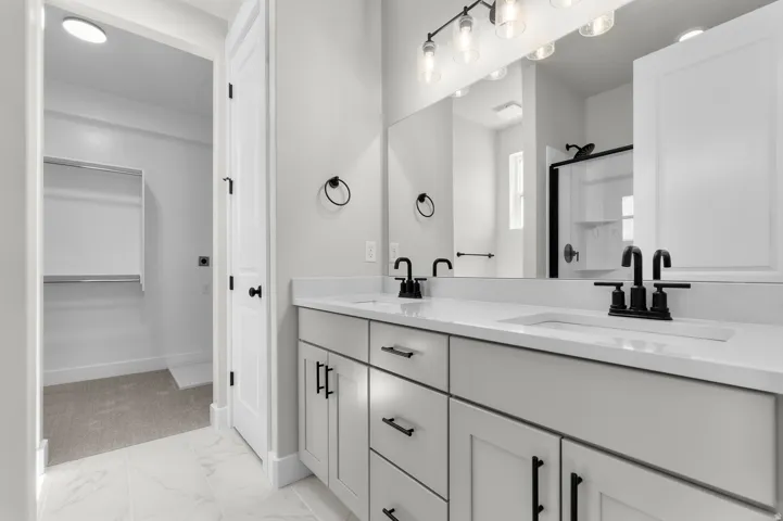 Bathroom featuring a double vanity with white countertops and matte black fixtures, an illuminated mirror, and a built-in shower with a glass enclosure