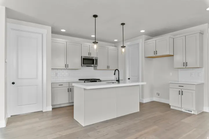 Contemporary kitchen featuring a central island with a sink, light-toned cabinetry, subway tile backsplash, stainless steel microwave, and wood-finish flooring