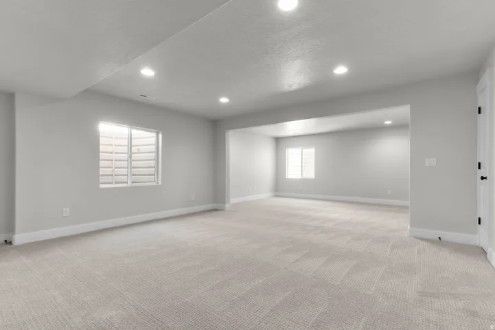 Spacious lower-level room featuring light neutral carpeting, recessed lighting, and two egress windows