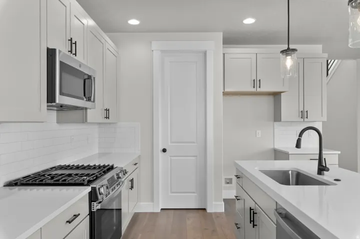 Contemporary kitchen featuring an island with an undermount sink, white shaker cabinetry, stainless steel appliances, and a subway tile backsplash