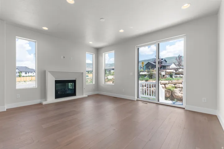 Spacious room with light wood-finish flooring, a contemporary fireplace with a white surround, and recessed ceiling lighting