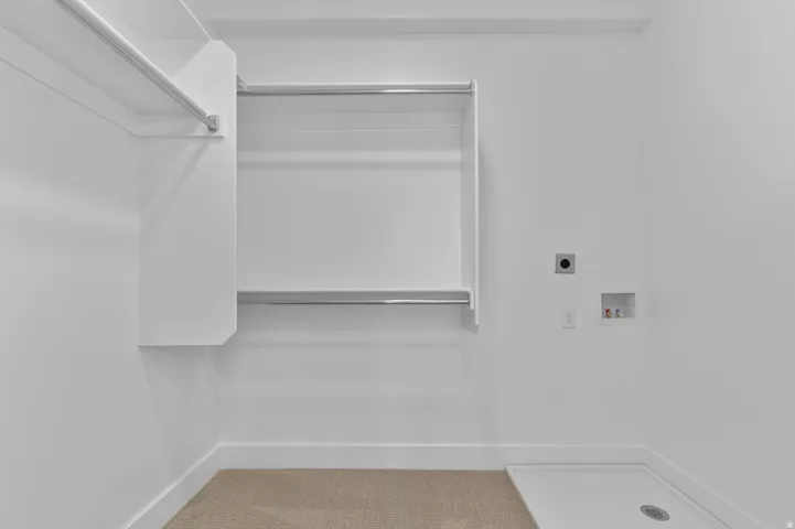 Laundry area featuring a dedicated floor drain, washer/dryer hookups, and built-in shelving with hanging rods