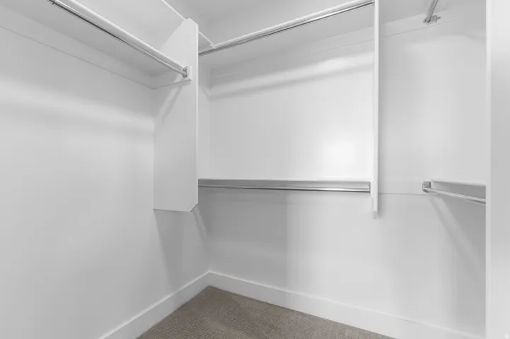 Walk-in closet featuring white built-in shelving, multiple hanging rods, and neutral-toned carpeting