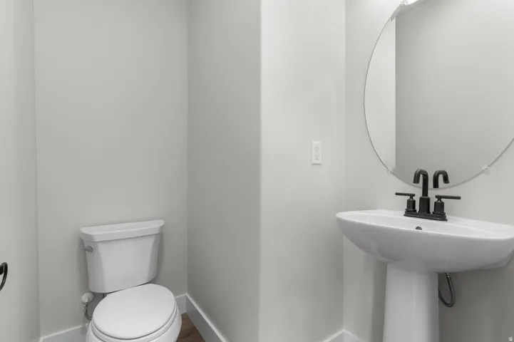 White pedestal sink with matte black faucet, illuminated by a circular mirror