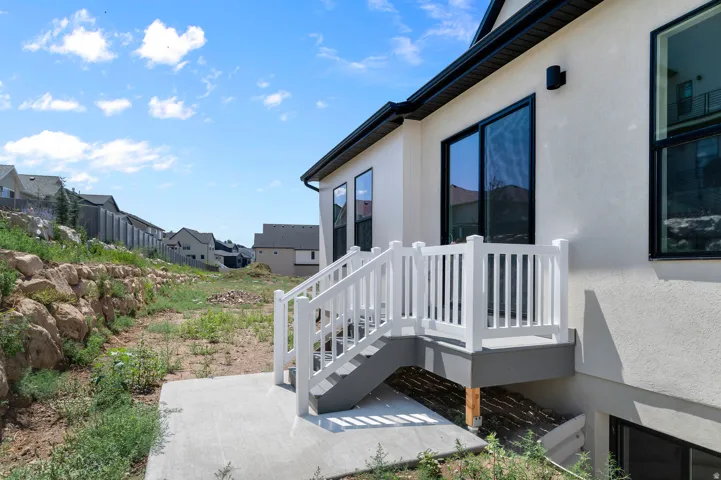Rear exterior featuring a deck with white railings and gray steps, a sliding glass door, multiple large windows with black frames, and a textured stucco finish
