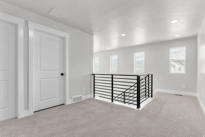 Carpeted upper-level landing featuring a contemporary black metal horizontal bar railing, multiple tall windows, recessed lighting, and white paneled doors
