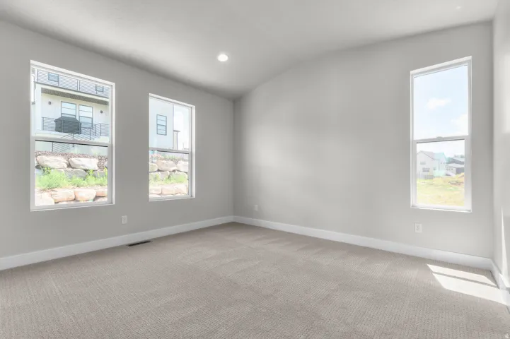 Spacious room with light-toned walls and plush carpeting, featuring three large windows for abundant natural light