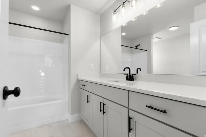 Bathroom featuring a light-toned vanity with an integrated sink and matte black faucet, a large frameless mirror, and a linear vanity light fixture