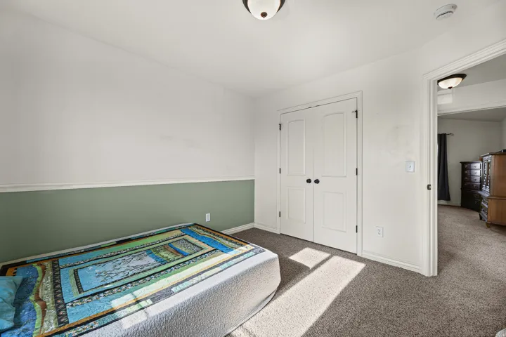 Bedroom featuring carpet flooring, two-tone painted walls with chair rail molding, and a double-door closet with black hardware