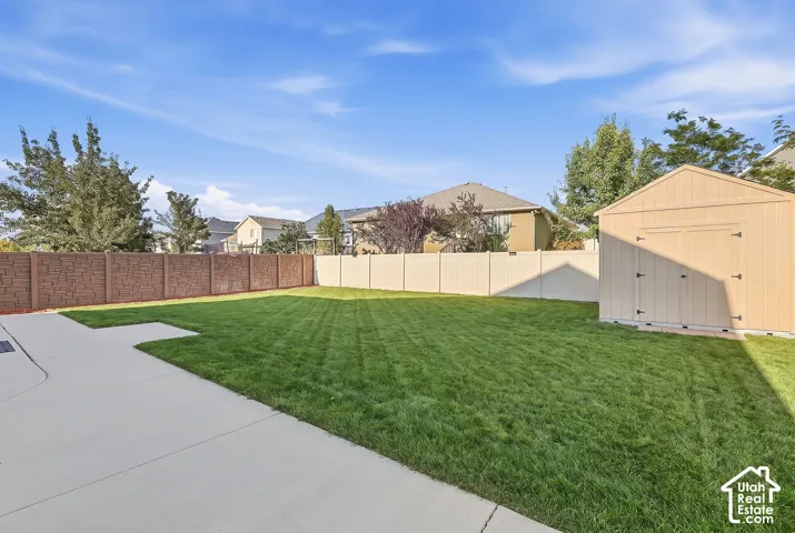 Expansive backyard featuring a large concrete patio, lush green lawn, and a durable storage shed