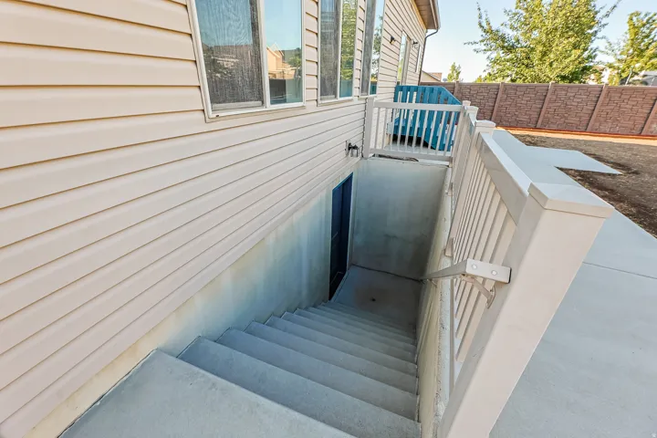 Concrete basement entrance featuring a handrail and vinyl siding exterior