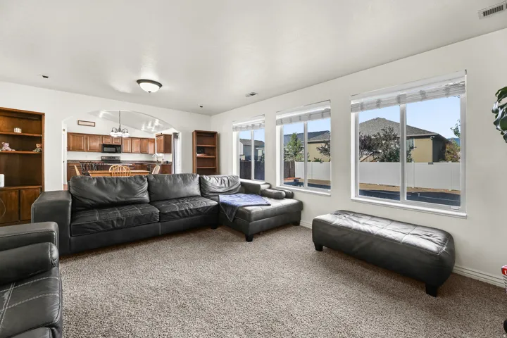 Carpeted living area featuring multiple windows, built-in shelving, and an arched entryway leading to the kitchen with wood cabinetry