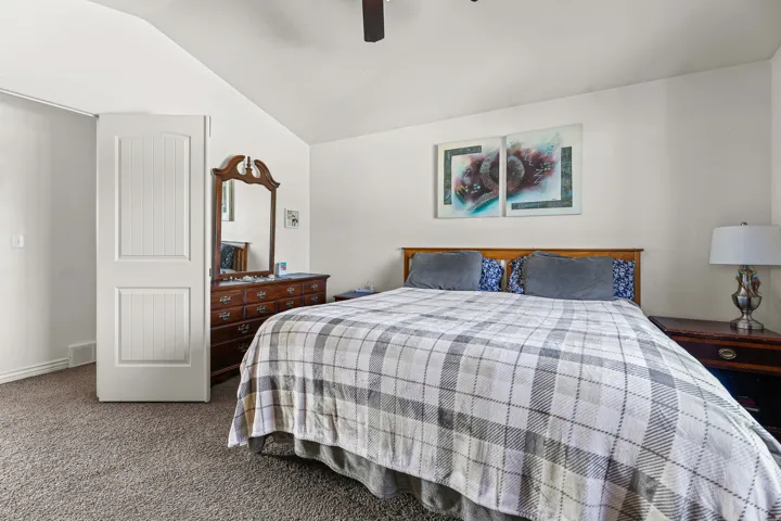 Bedroom featuring vaulted ceilings, carpet flooring, a ceiling fan, and a paneled door