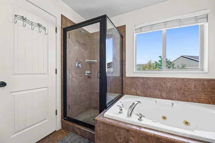 Tiled shower enclosure with a clear glass door, a separate jetted soaking tub, and a window with horizontal blinds