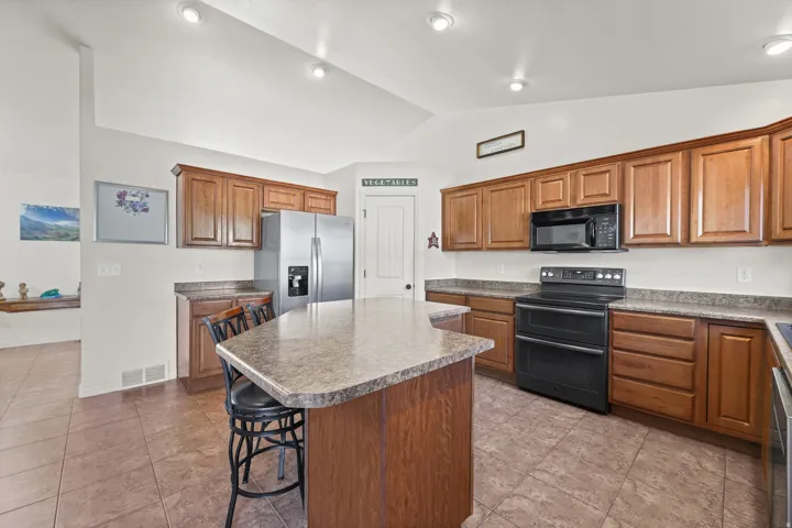 Kitchen featuring a central island with countertop seating, wood-finish cabinetry, granite-finish countertops, and stainless steel appliances