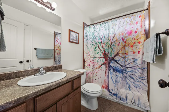 Bathroom featuring a wood-finish vanity with a built-in sink, a speckled countertop, a large wall mirror, and a toilet