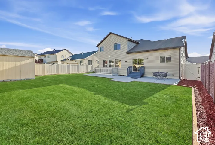 Expansive grassy yard featuring a multi-level concrete patio, direct house access, and a dedicated storage shed