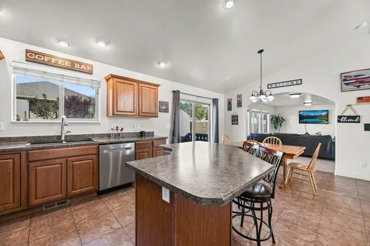 Kitchen featuring a central island with bar seating, wood cabinetry, stainless steel dishwasher, and a double basin sink