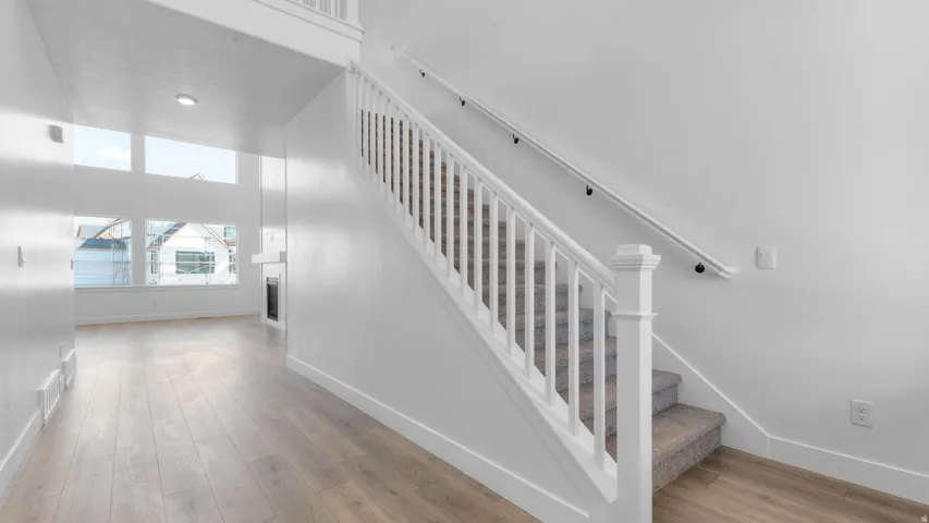 Two-story entry featuring light wood-finish flooring, a white spindle staircase with carpeted treads, and high ceilings