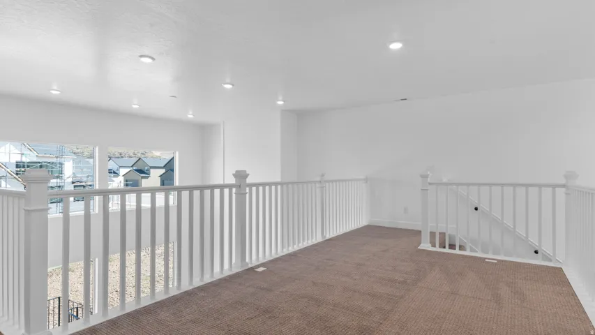 Carpeted loft area featuring white painted railings with detailed newel posts, recessed lighting, and multiple windows