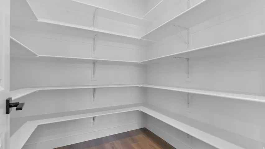 Spacious walk-in pantry featuring white shelving, white walls, and wood-finish flooring