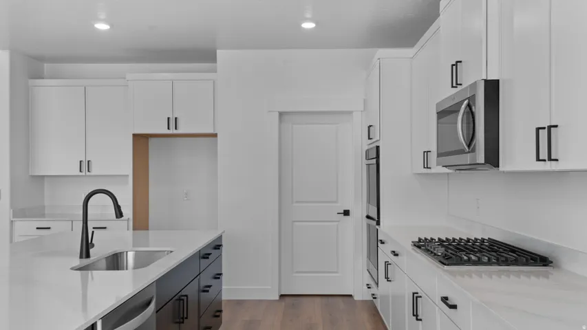 Contemporary kitchen featuring white cabinetry, a large island with an undermount sink and matte black faucet, integrated stainless steel appliances, and wood-finish flooring