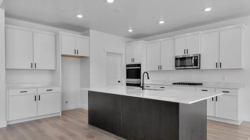 Spacious kitchen featuring a dark wood-finish island with white countertop, white cabinetry with dark hardware, recessed lighting, and wood-finish flooring
