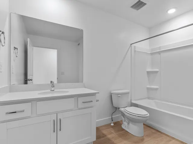 Bathroom featuring a white vanity with a light-toned countertop, a rectangular mirror, and a white bathtub with shower surround