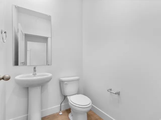 Pedestal sink with chrome faucet, wall-mounted mirror, white toilet, and light wood-finish flooring