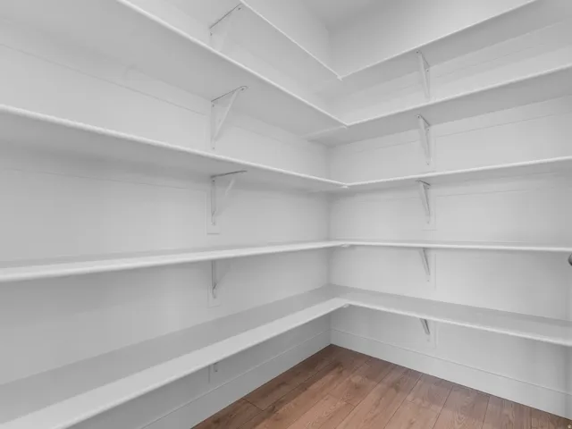 Spacious walk-in pantry featuring white walls, extensive white shelving, and wood-finish flooring