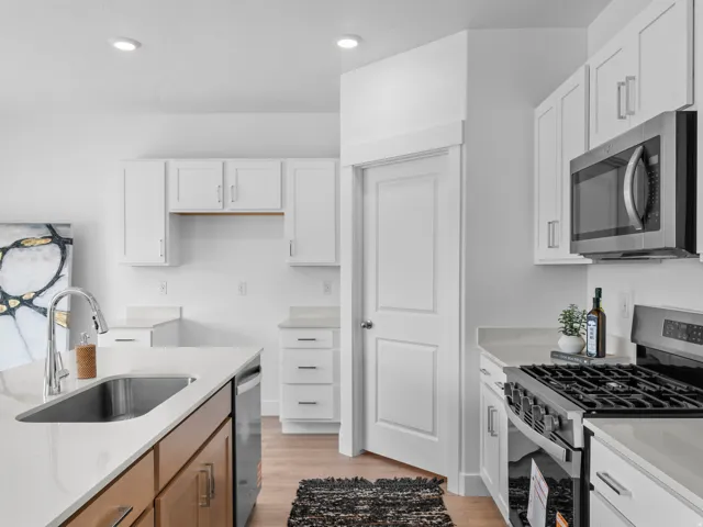 Modern kitchen featuring white shaker cabinetry, light-toned countertops, a stainless steel gas range, and a built-in microwave