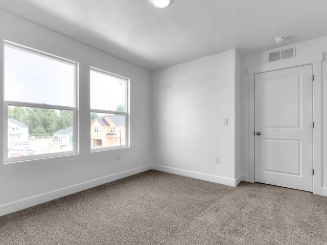 Carpeted room featuring two large windows, a white paneled door, ceiling-mounted lighting, and crisp white trim