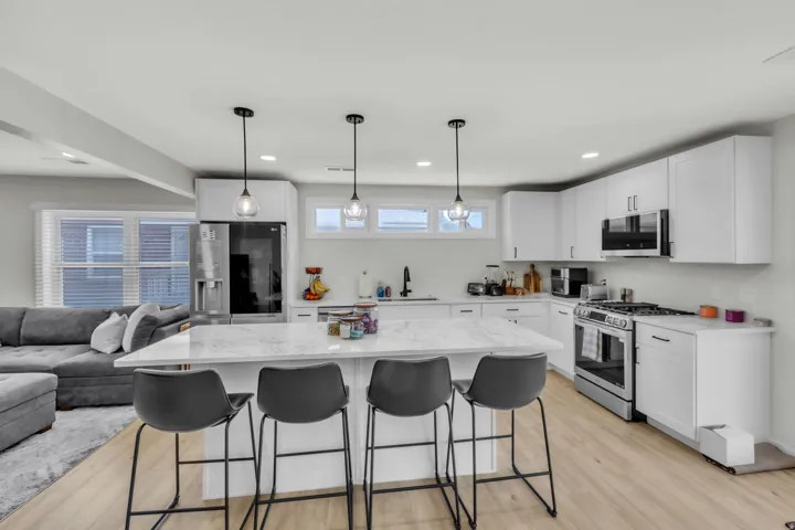 Contemporary kitchen featuring a large central island with seating, white shaker-style cabinetry, stainless steel appliances, and a gas range