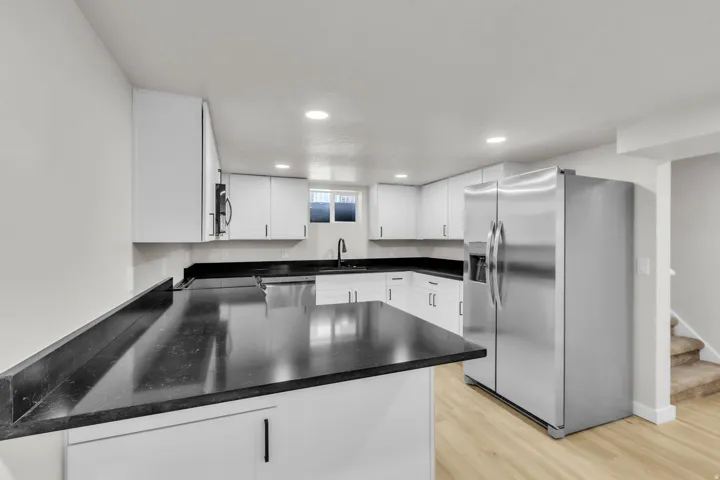 Modern kitchen featuring white cabinetry, dark countertops, stainless steel refrigerator, recessed lighting, and light wood-finish flooring