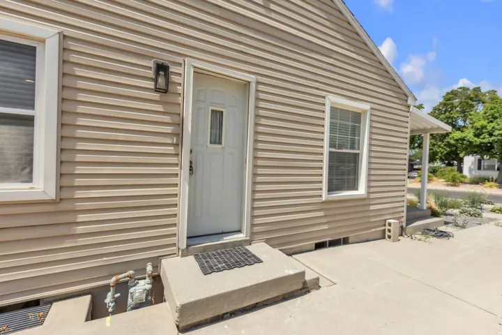 Beige horizontal siding exterior featuring a white paneled entry door with a window insert