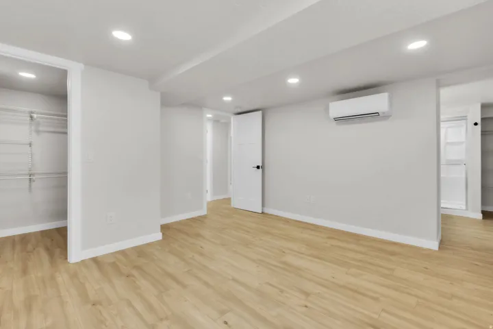 Spacious interior room featuring light wood-finish flooring, recessed lighting, and a wall-mounted mini-split HVAC unit