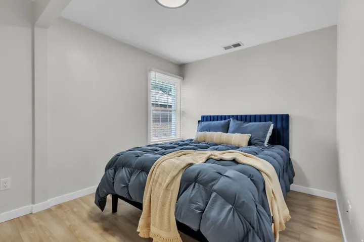 Bedroom with light-toned walls, a window featuring white blinds, wood-finish flooring, a white ceiling, and white baseboards