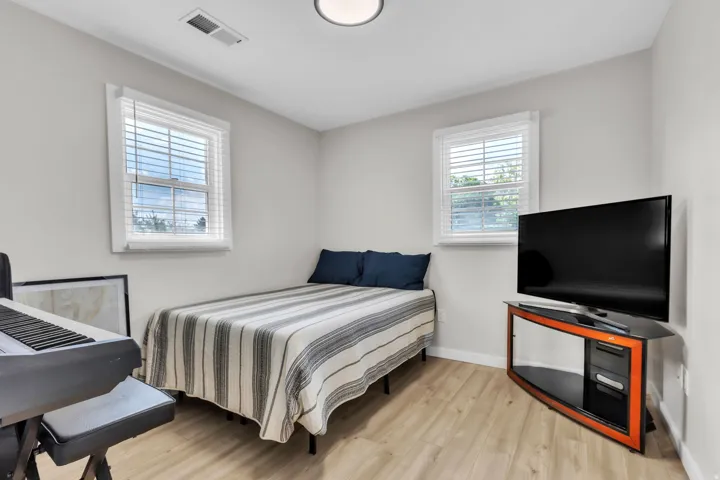 Light-toned wood-finish flooring complements the neutral wall color in this space, featuring two windows with white blinds, a ceiling-mounted light fixture, and crown molding