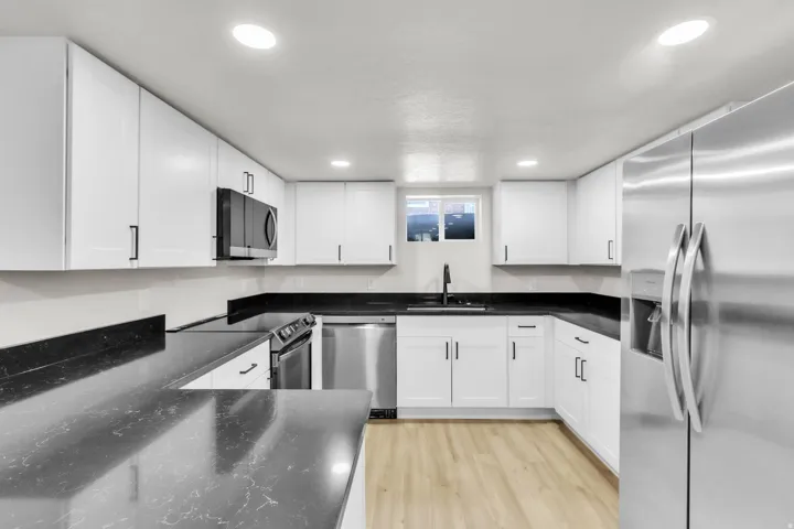 Modern kitchen featuring white shaker cabinetry, dark countertops, stainless steel appliances, and wood-finish flooring