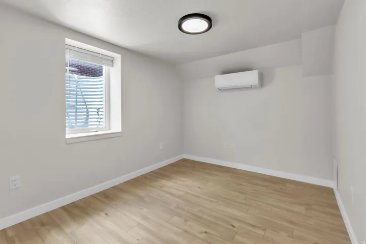Light-filled room featuring wood-finish flooring, a wall-mounted mini-split HVAC unit, a flush-mount ceiling light fixture, and white baseboards