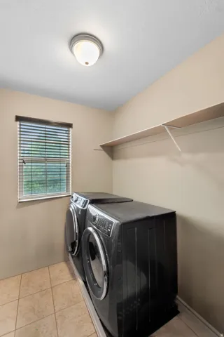 Laundry room featuring neutral wall paint, tile flooring, a window with blinds, and an overhead light fixture