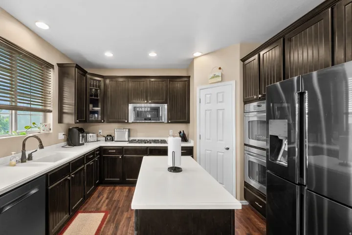 Spacious kitchen featuring rich dark cabinetry, light countertops, wood-finish flooring, a built-in double oven, and recessed lighting